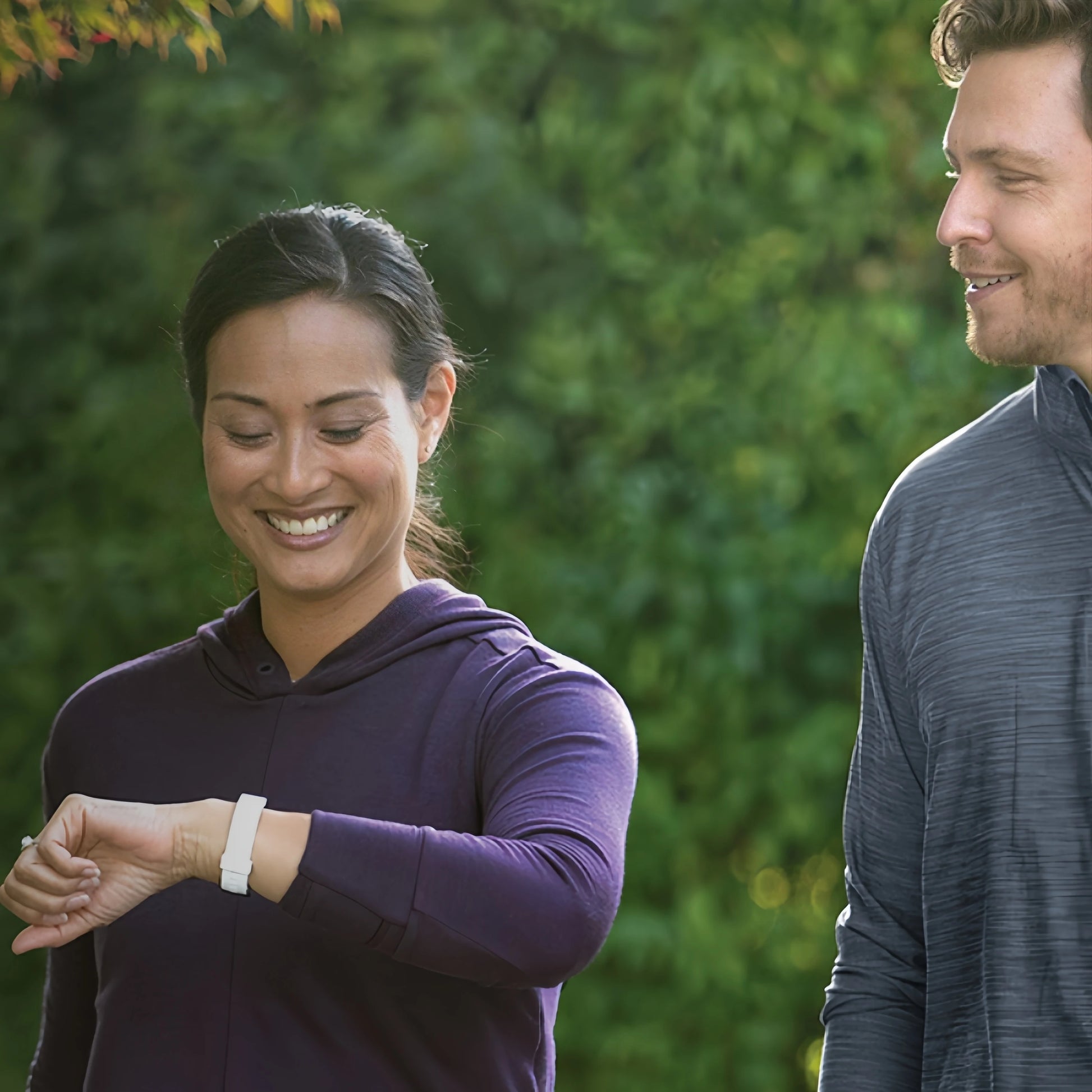 Woman wearing a waterproof heart rate smart band checking fitness data outdoors with a man nearby