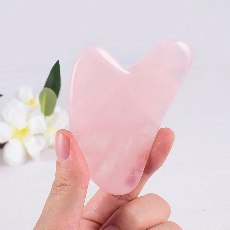 Hand holding a pink natural stone gua sha facial tool with white flowers in the background