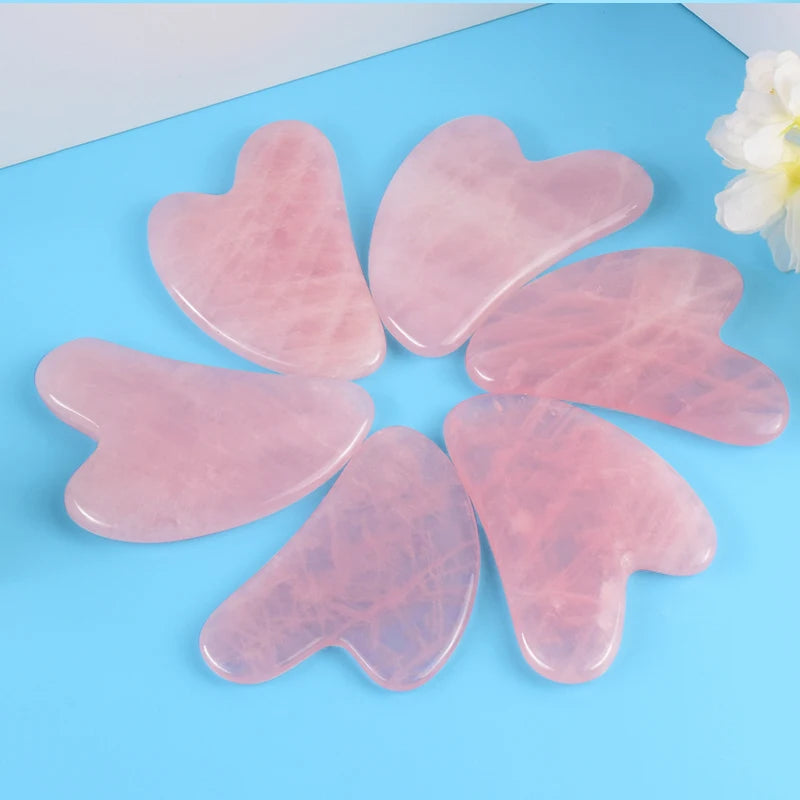 Set of six pink rose quartz natural stone gua sha facial tools arranged on blue surface