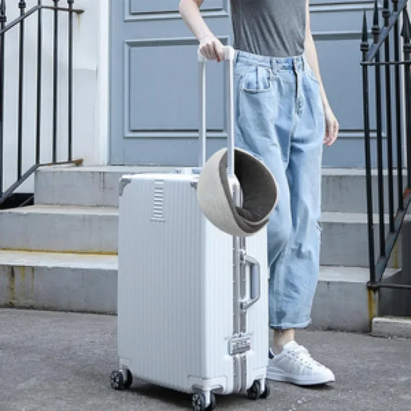 Person holding a white rolling suitcase with a gray memory foam travel neck pillow attached