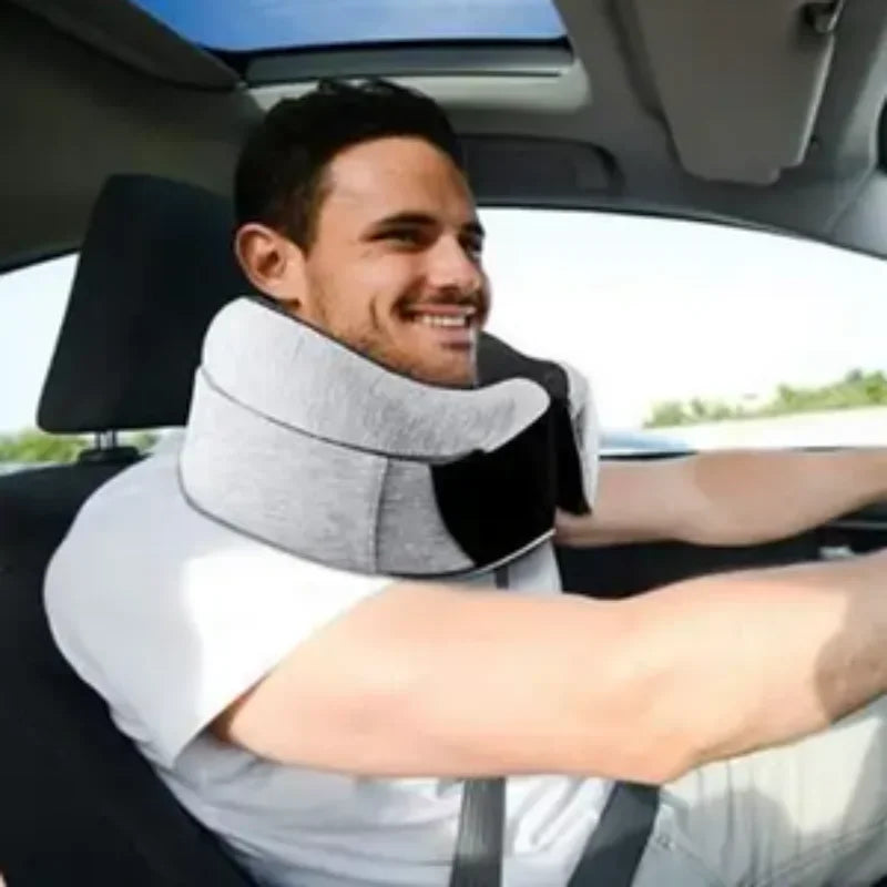 Man wearing gray memory foam travel neck pillow while sitting and smiling in a car seat