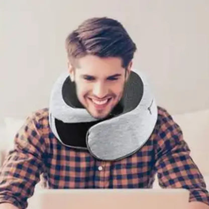 Man wearing a grey memory foam travel neck pillow while smiling and using a laptop