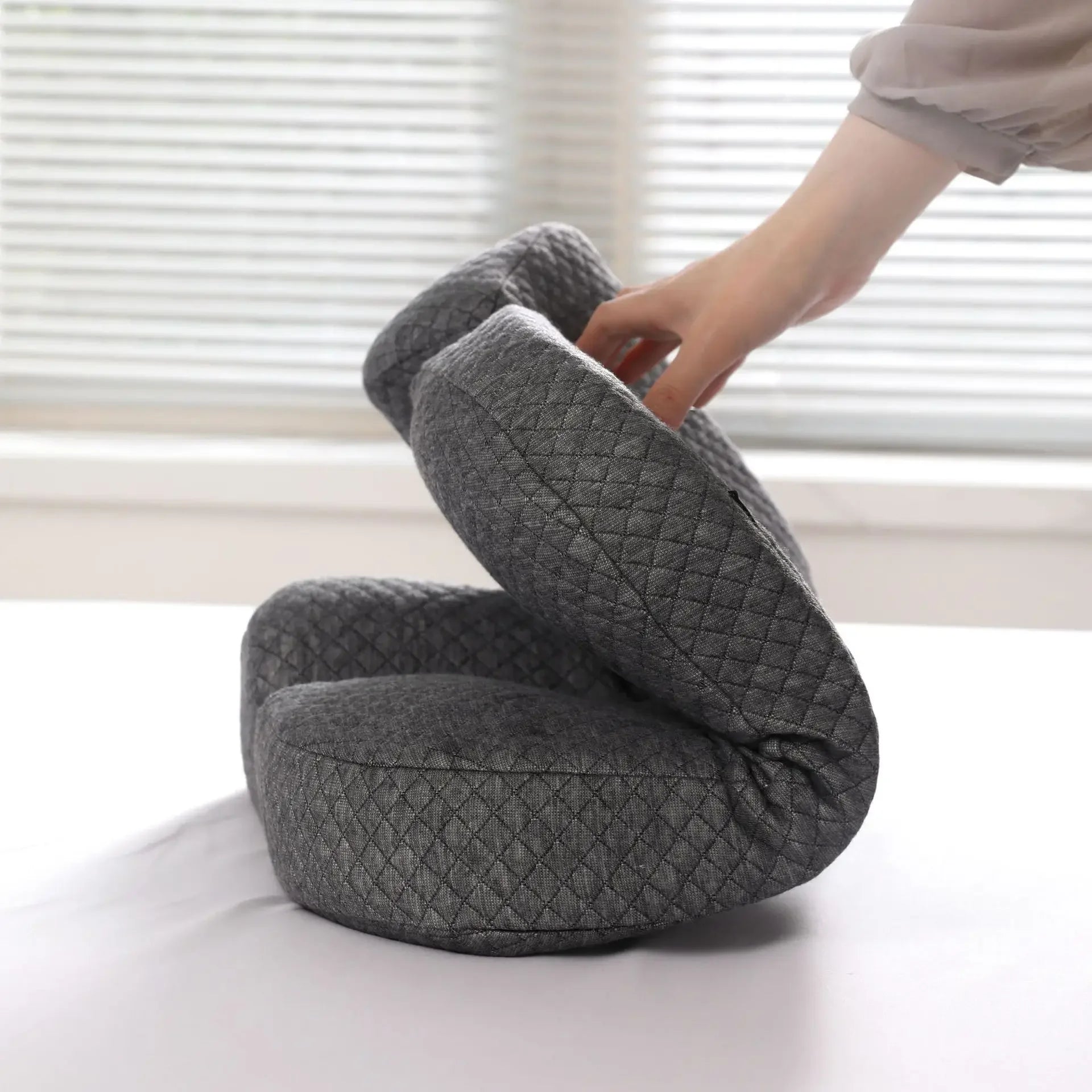 Hand holding a foldable gray orthopedic memory foam pillow with quilted texture on white surface