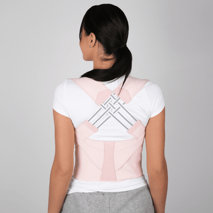 Back view of woman wearing Zorelie adjustable posture corrector in light pink over white shirt