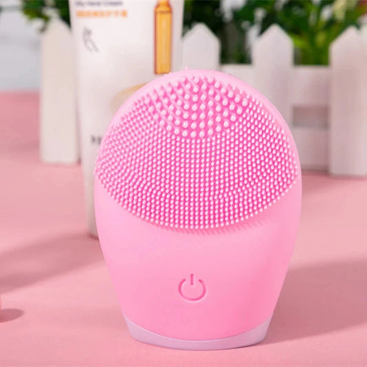 Pink silicone facial cleansing brush with soft bristles and power button on a pink surface