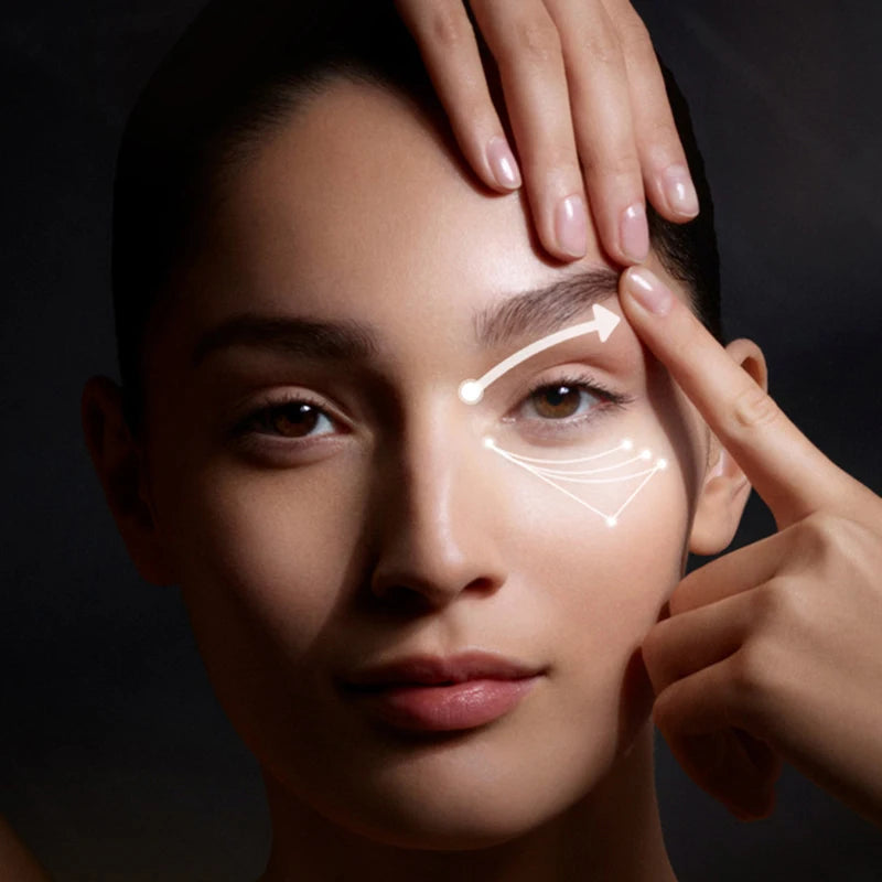 Woman demonstrating application of 24k gold eye cream with glowing effect around eye area